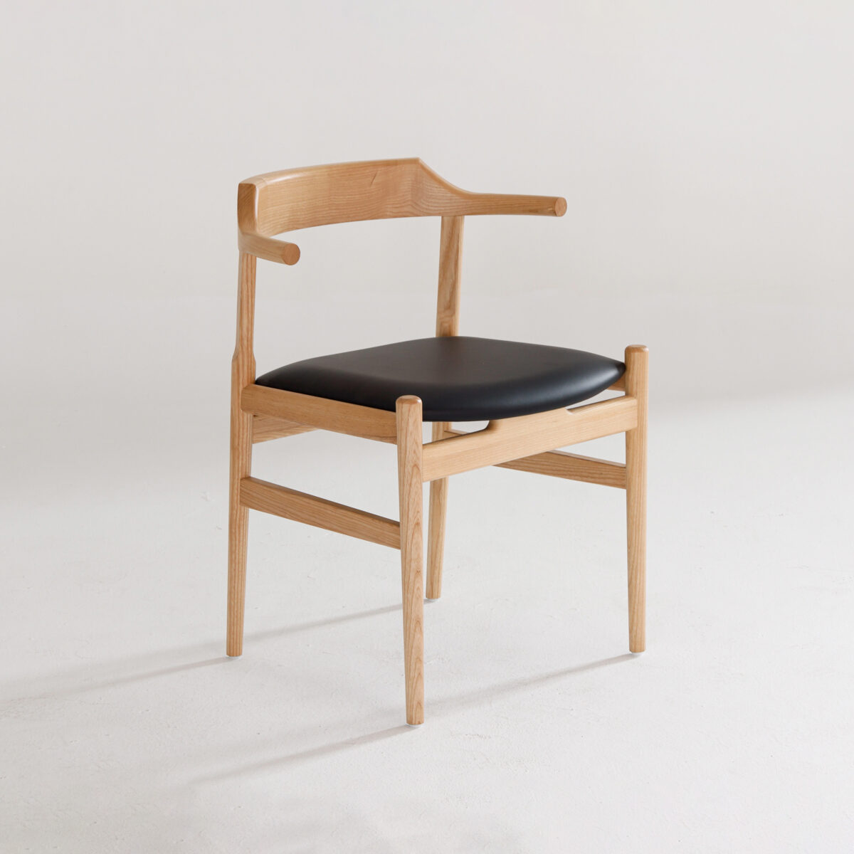 Final Chair_B10 A modern wooden chair with a light wood frame, curved backrest, and a black cushioned seat, positioned on a white floor against a plain white background.