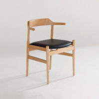 A modern wooden chair with a light wood frame, curved backrest, and a black cushioned seat, positioned on a white floor against a plain white background.