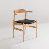 A modern wooden chair with a light wood frame, curved backrest, and a black cushioned seat, positioned on a white floor against a plain white background.