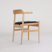 A modern wooden chair with a light wood frame, a curved backrest, and a black upholstered seat, set against a plain white background.