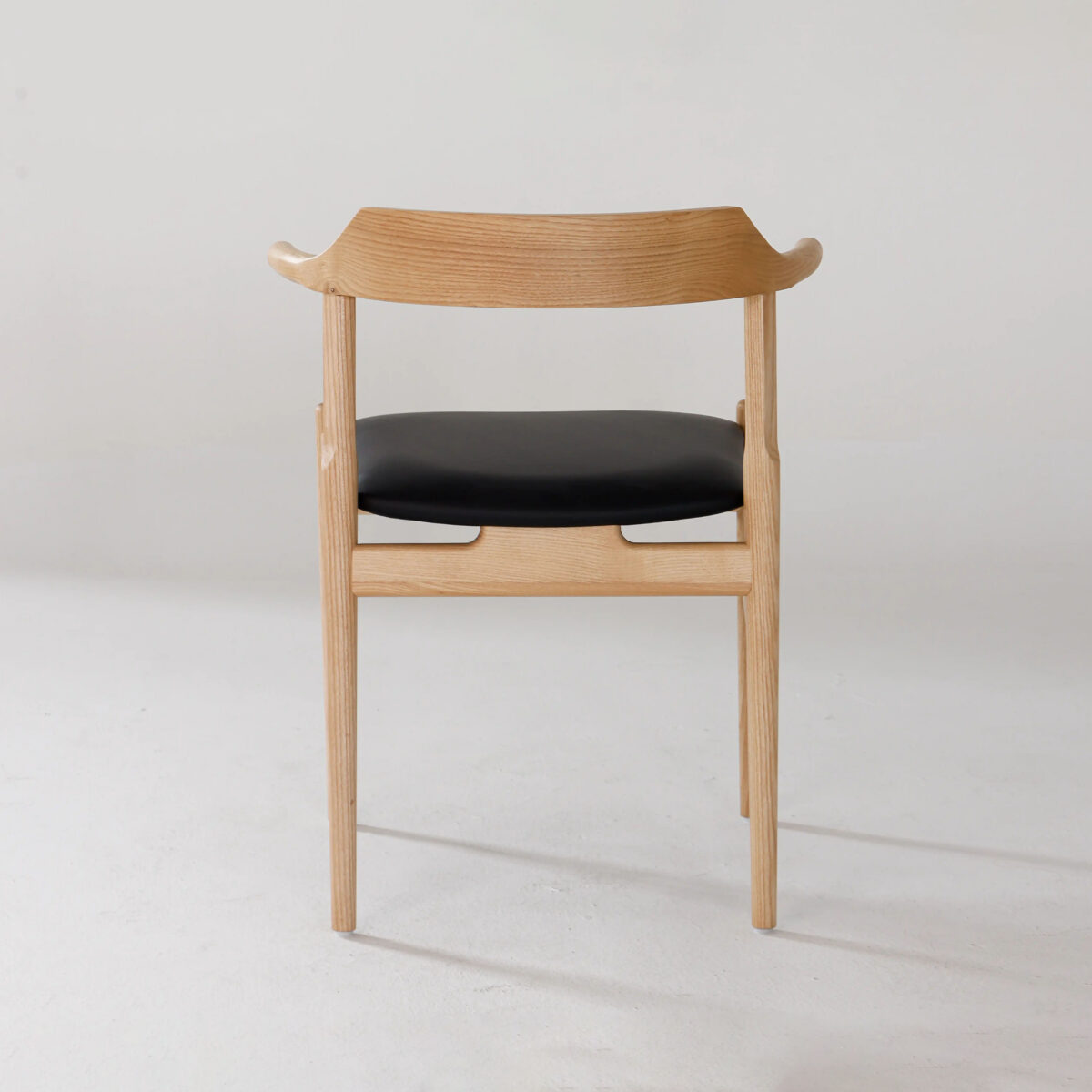 Final Chair_B3 A wooden chair with a curved backrest and black cushioned seat, shown from the back against a plain white background. The design is minimal and modern.