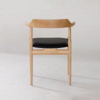 A wooden chair with a curved backrest and black cushioned seat, shown from the back against a plain white background. The design is minimal and modern.