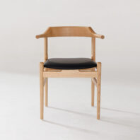 A modern wooden chair with light-coloured wood, curved armrests, and a black cushioned seat, set against a plain white background.