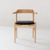 A modern wooden chair with light-coloured wood, curved armrests, and a black cushioned seat, set against a plain white background.