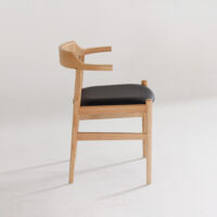 A modern wooden chair with a curved backrest and armrests, featuring a black upholstered seat, is shown against a plain white background. The chair is viewed from the side.