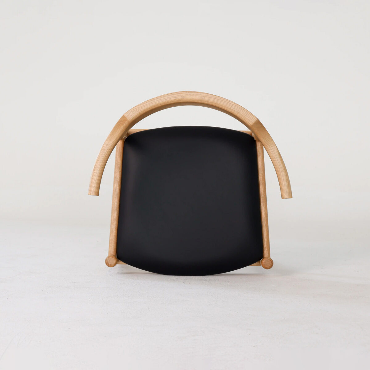 Final Chair_B9 A modern chair with a curved light wood frame and a black seat, photographed against a plain white background. The chair is positioned facing forward, showcasing its minimalist and unique design.