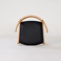 A modern chair with a curved light wood frame and a black seat, photographed against a plain white background. The chair is positioned facing forward, showcasing its minimalist and unique design.