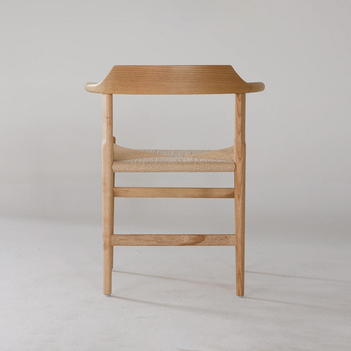 Final Chair_Paper Robe_B2 A wooden chair with a curved backrest and a woven seat, photographed from the back against a plain, light-coloured background. The design is minimalistic and modern.