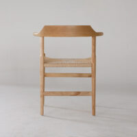 A wooden chair with a curved backrest and a woven seat, photographed from the back against a plain, light-coloured background. The design is minimalistic and modern.