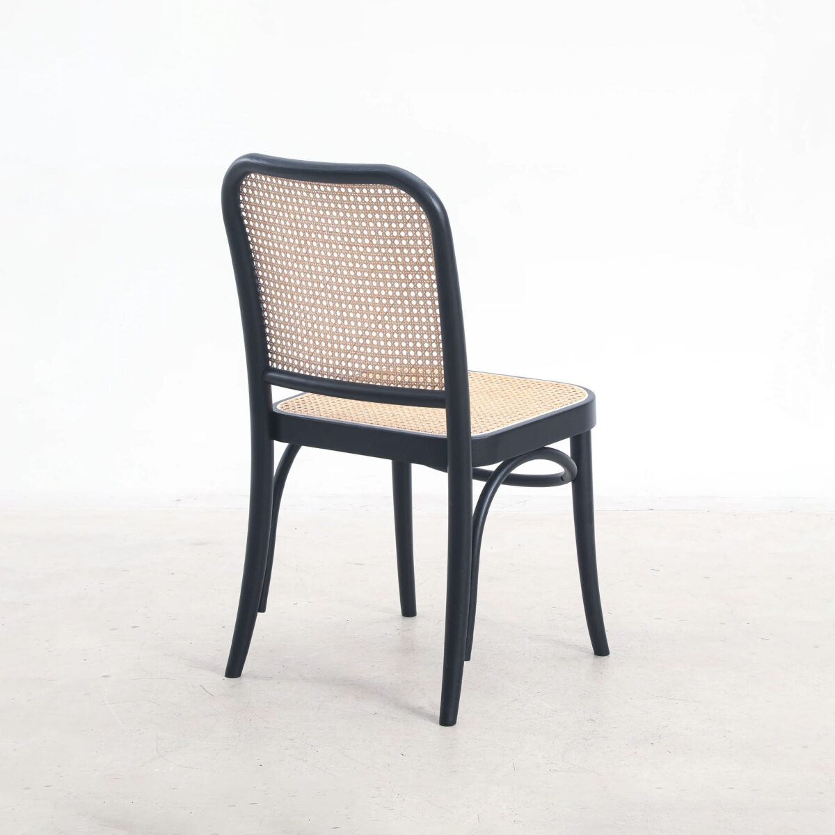 Rattan_B1 A black wooden chair with a woven rattan seat and backrest, shown on a light, plain background. The chair is angled so the back and one side are visible.