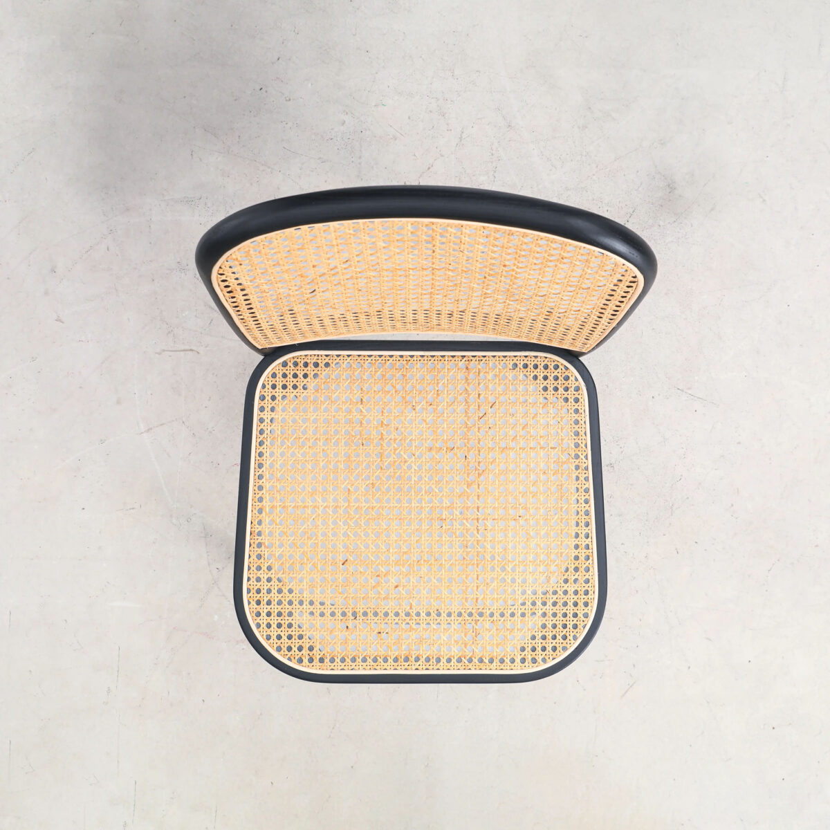 Rattan_B10 Top-down view of a chair with a black frame and woven rattan seat and backrest, placed on a light, smooth surface.