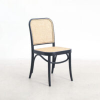 A black-framed chair with a woven cane seat and backrest is positioned on a light-coloured floor against a plain white background.