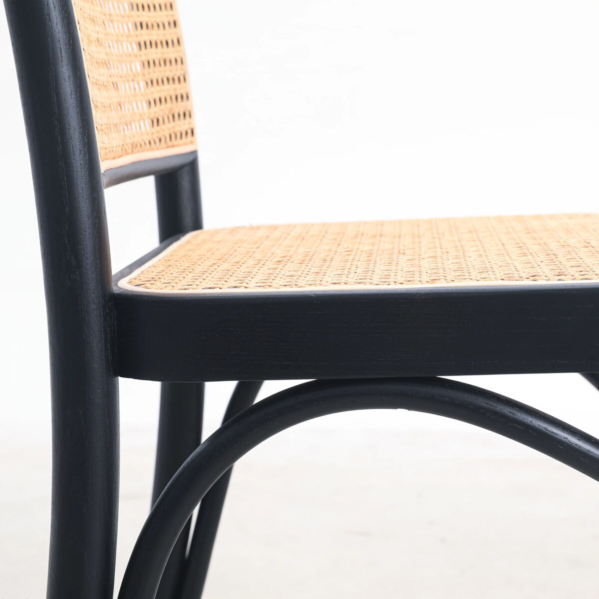 Rattan_B3 Close-up of a chair with a black wooden frame and a woven cane seat and backrest, set against a plain white background.