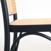 Close-up of a chair with a black wooden frame and a woven cane seat and backrest, set against a plain white background.