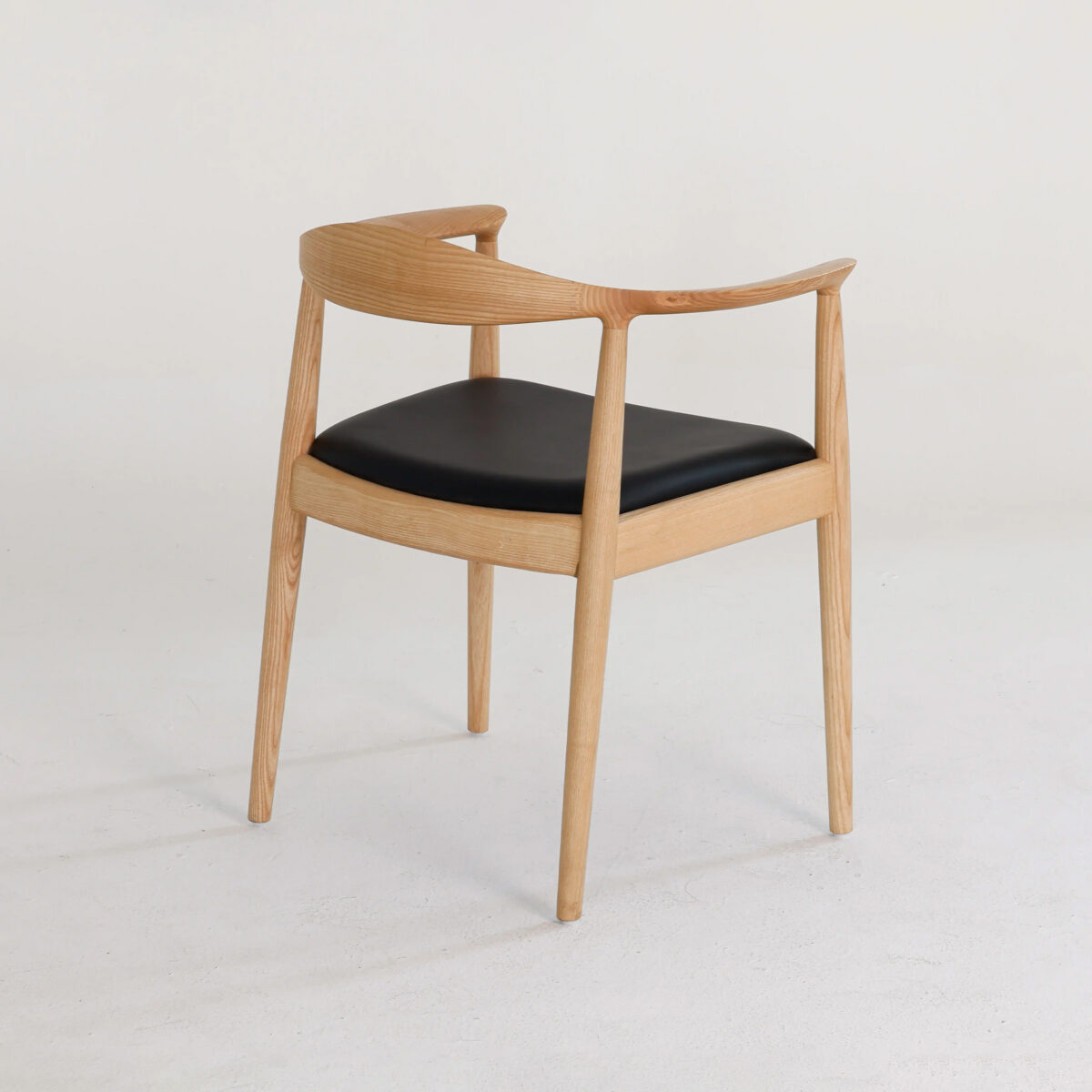 Round Chair_Leather_B1 A modern wooden chair with a curved backrest and armrests, featuring a black cushioned seat. The chair is set against a plain, light-coloured background.