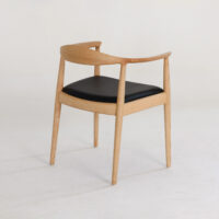 A modern wooden chair with a curved backrest and armrests, featuring a black cushioned seat. The chair is set against a plain, light-coloured background.