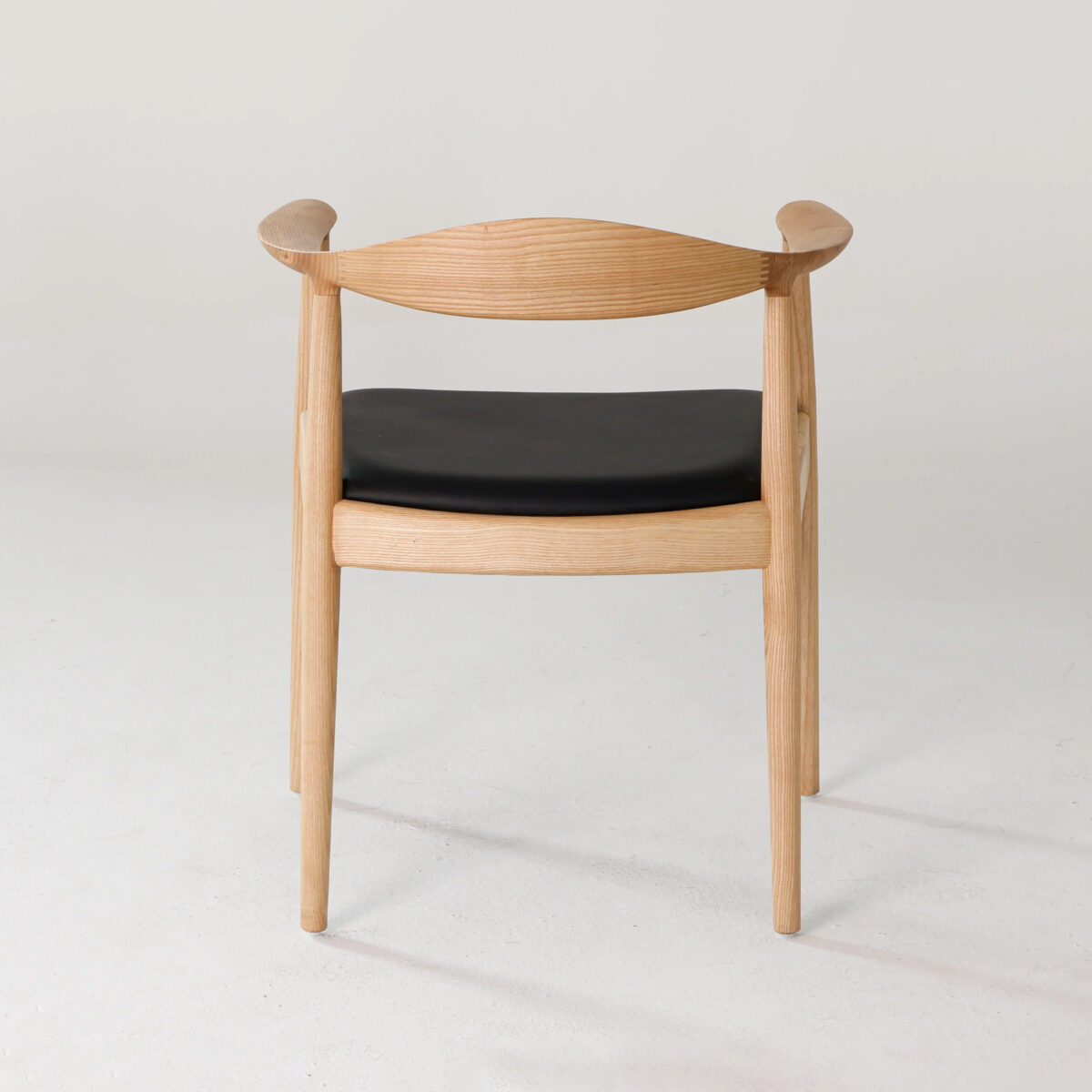 Round Chair_Leather_B2 A wooden chair with curved armrests and a black cushioned seat, viewed from the back, set against a plain light-coloured background.