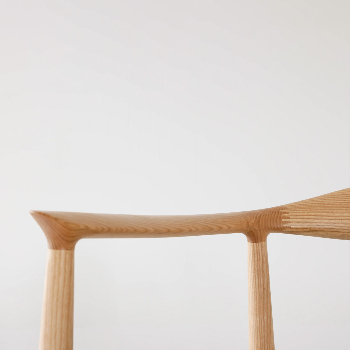 Round Chair_Leather_B3 Minimalist close-up of a wooden chair’s backrest and legs, featuring smooth, natural wood grain against a plain white background.