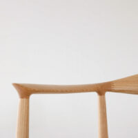 Minimalist close-up of a wooden chair’s backrest and legs, featuring smooth, natural wood grain against a plain white background.