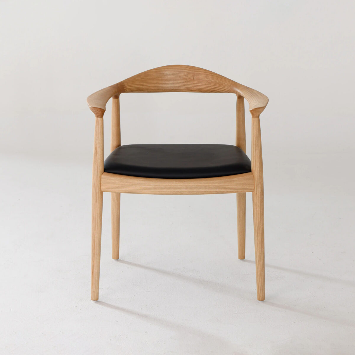 Round Chair_Leather_B6 A modern wooden chair with a curved backrest, open sides, and a black cushioned seat, placed against a plain white background.