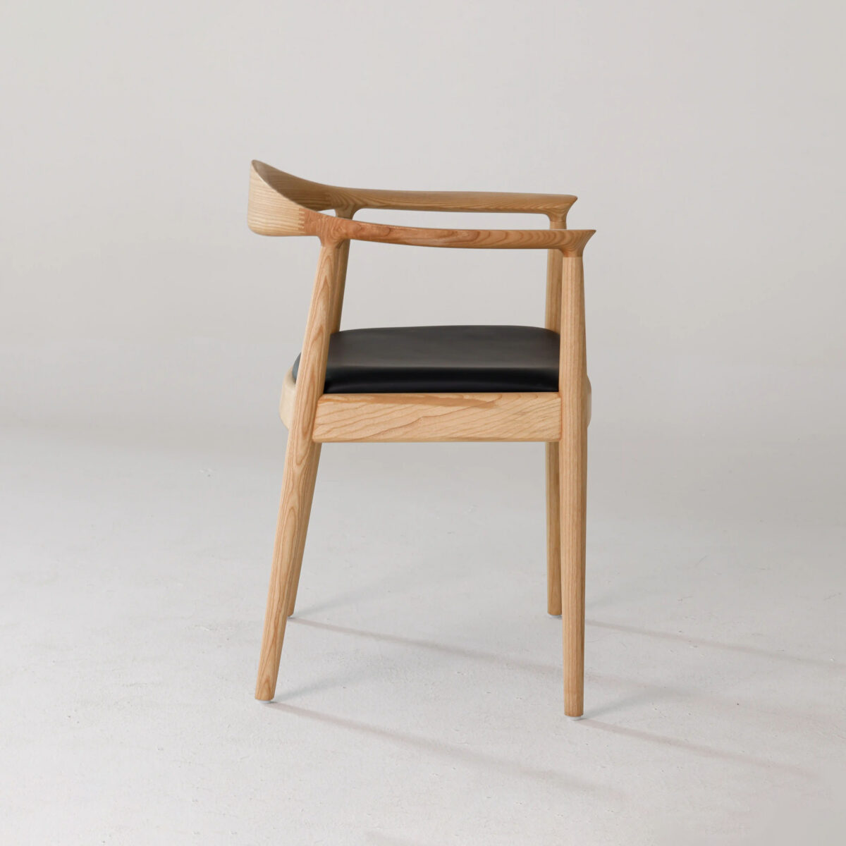 Round Chair_Leather_B7 A modern wooden chair with a curved backrest, angled armrests, and a black cushioned seat is shown on a plain white background.