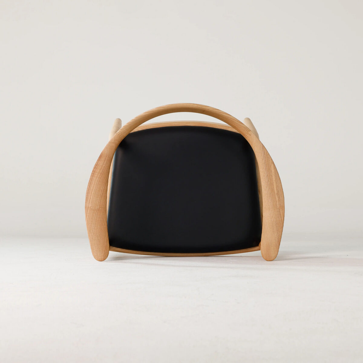 Round Chair_Leather_B8 A modern chair with a curved wooden frame and a black cushioned seat, photographed from the front against a plain, light background.