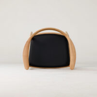 A modern chair with a curved wooden frame and a black cushioned seat, photographed from the front against a plain, light background.
