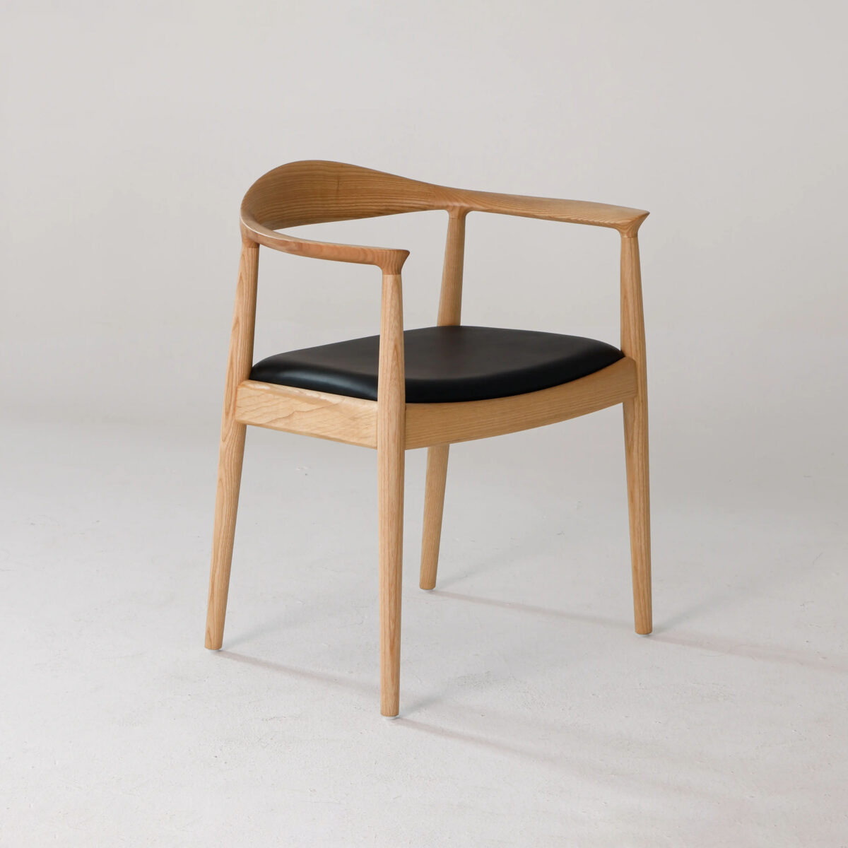 Round Chair_Leather_B9 A minimalist wooden chair with a curved backrest and black cushioned seat, set against a plain light background. The design features clean lines and a natural wood finish.