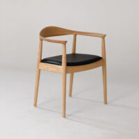 A minimalist wooden chair with a curved backrest and black cushioned seat, set against a plain light background. The design features clean lines and a natural wood finish.