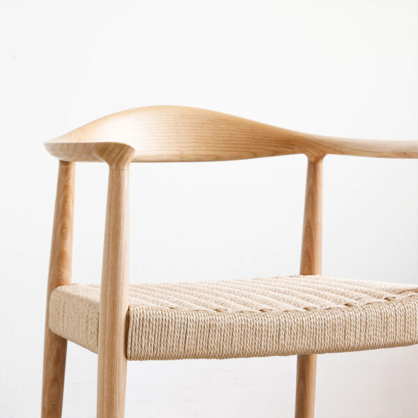 A minimalist wooden chair with a curved backrest and woven natural seat, set against a plain white background. The design features smooth, rounded edges and clean lines, showcasing Scandinavian-inspired craftsmanship.