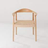 A minimalist wooden chair with a curved backrest and woven seat, set against a plain white background. The design features smooth, rounded edges and clean lines, giving it a modern, Scandinavian look.