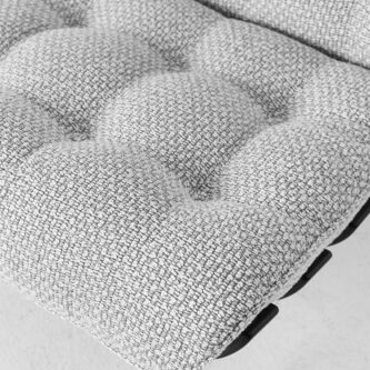 Close-up of a light grey textured upholstered cushion with deep tufting, shown on a black metal-framed chair.
