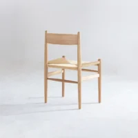 A minimalist wooden chair with a woven seat and a simple, angular design, placed on a light, plain background.