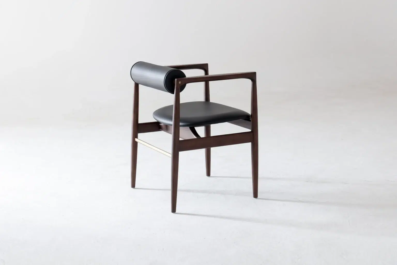 Back side view A modern chair with a dark wooden frame, black leather seat, and a cylindrical black leather headrest, positioned against a plain light background.