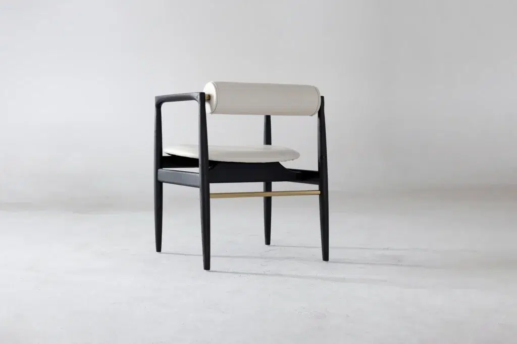 A modern chair with slender black legs, a round white cushioned seat, and a cylindrical white padded backrest, set against a plain light grey background. The chair features minimalistic and elegant design lines.