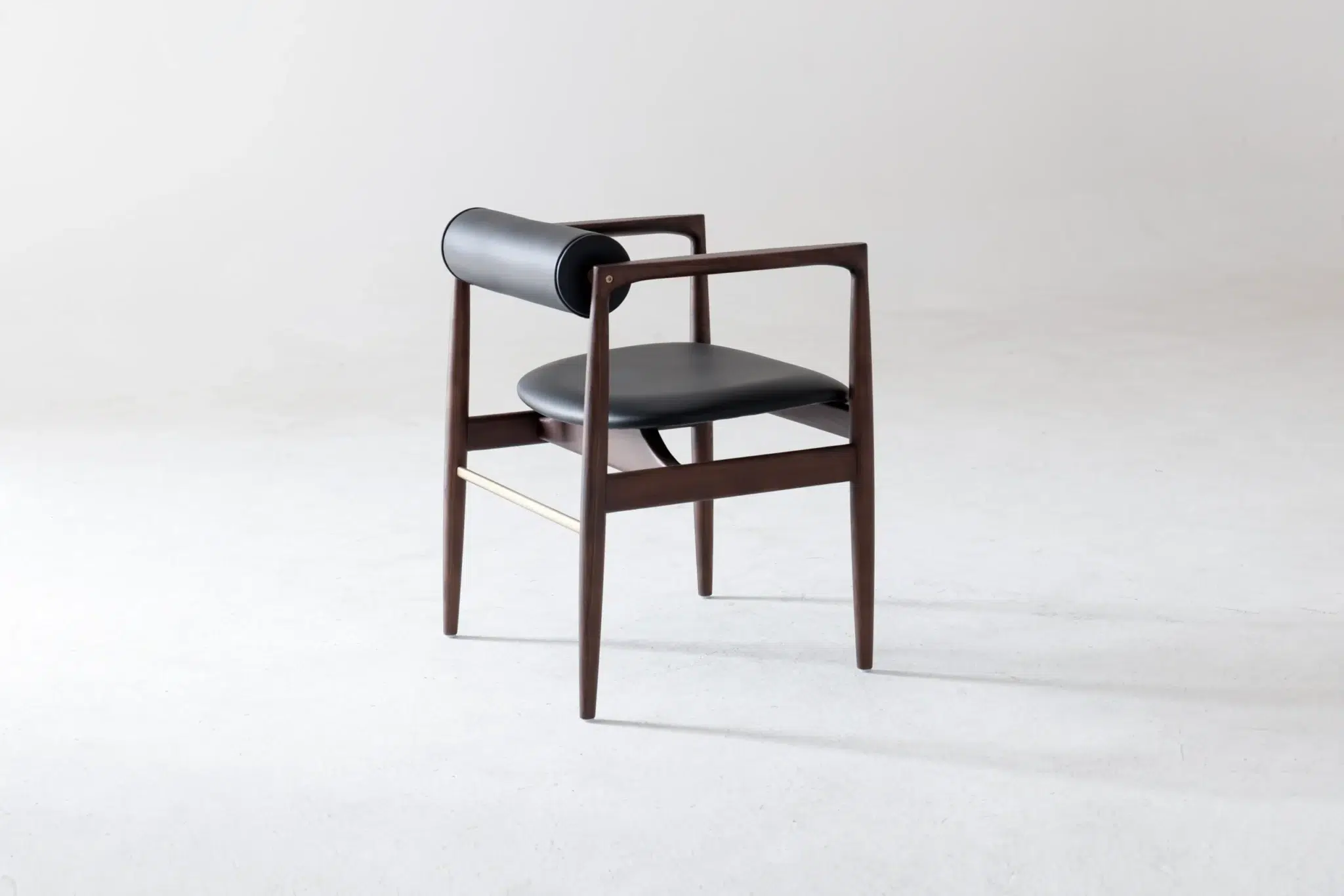 A modern wooden chair with a dark finish, black leather seat, and cylindrical black leather backrest, set against a plain light background.
