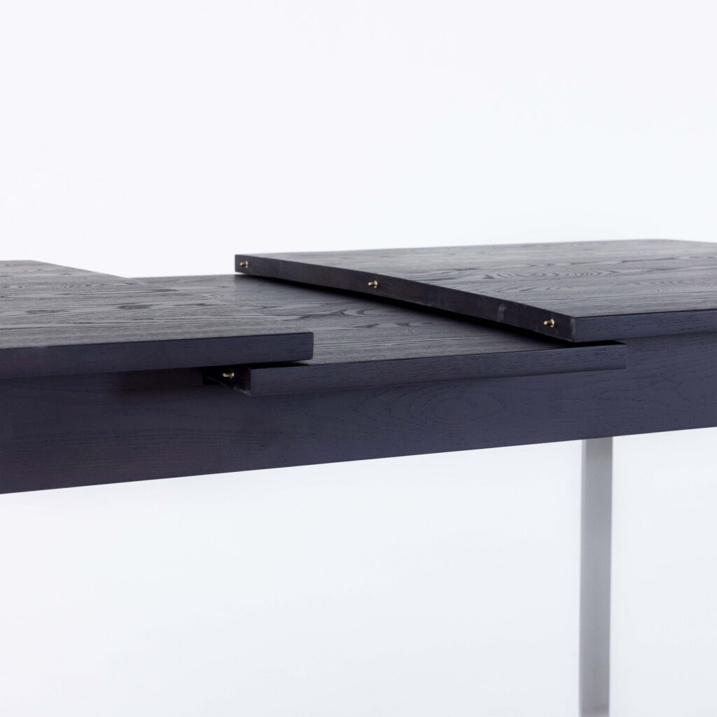 A close-up of a dark wooden table with a sliding extension mechanism. The tabletop sections are partially separated, showing how the extension piece fits between them. The background is plain white.