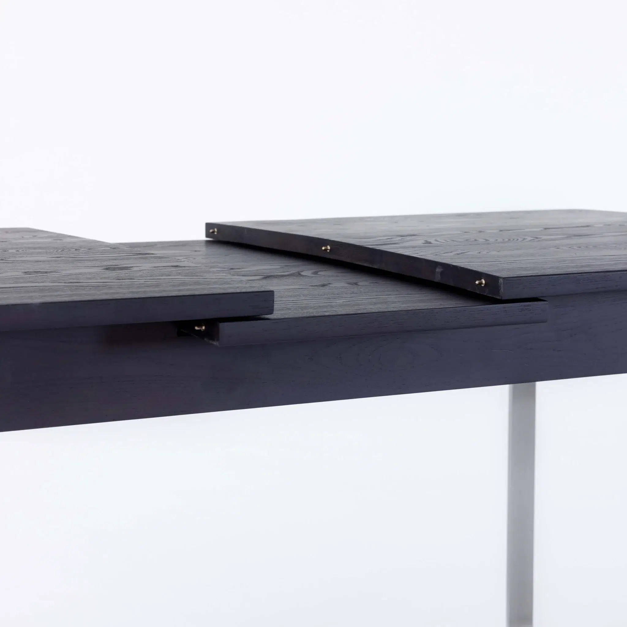 A close-up of a dark wooden table with extending leaves, showing the sliding mechanism and layered tabletop pieces against a plain white background.