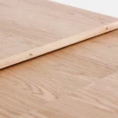 A close-up of a light wood surface with a wooden plank laid diagonally on top, secured with small brass screws. The wood has a natural grain pattern and a smooth finish.