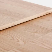 A close-up of a light wood surface with a wooden plank laid diagonally on top, secured with small brass screws. The wood has a natural grain pattern and a smooth finish.