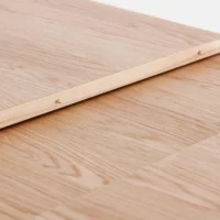 A close-up of a light wood surface with a wooden plank laid diagonally on top, secured with small brass screws. The wood has a natural grain pattern and a smooth finish.