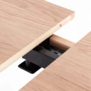 A close-up of a light wood extendable table showing the mechanism and gap where the table leaves join.