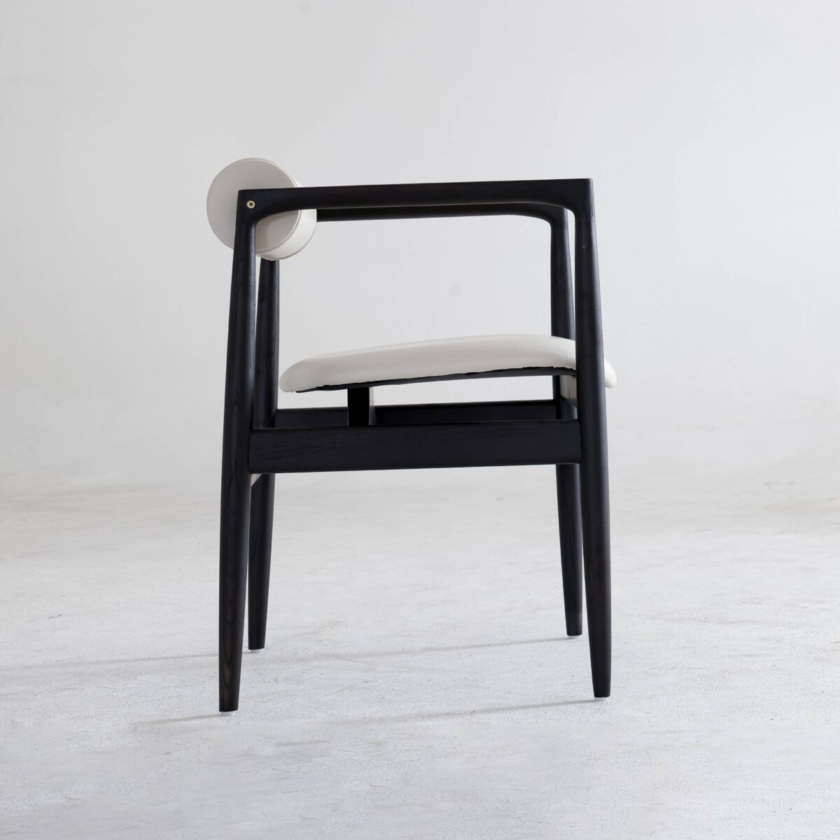 Black Frame + White Seat_B7 A modern chair with a black wooden frame, white cushioned seat, and a round white backrest, placed on a light grey floor against a plain white background.