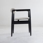 A modern chair with a black wooden frame, white cushioned seat, and a round white backrest, placed on a light grey floor against a plain white background.