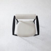 Top-down view of a modern chair with a round, white cushioned seat and backrest, and dark, curved wooden armrests on a light, textured floor.