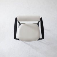 Top-down view of a modern chair with a round, white cushioned seat and backrest, and dark, curved wooden armrests on a light, textured floor.