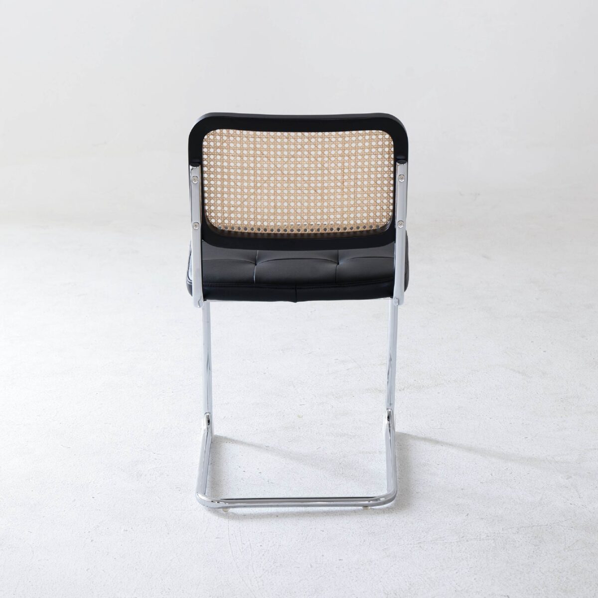 Black Frame_Chrome_Black Leather_B2 A modern chair with a chrome cantilever frame, black cushioned seat, and a backrest featuring a woven cane design, photographed against a plain white background.