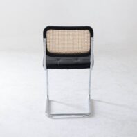 A modern chair with a chrome cantilever frame, black cushioned seat, and a backrest featuring a woven cane design, photographed against a plain white background.