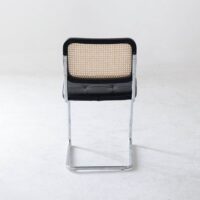 A modern chair with a chrome cantilever frame, black cushioned seat, and a backrest featuring a woven cane design, photographed against a plain white background.
