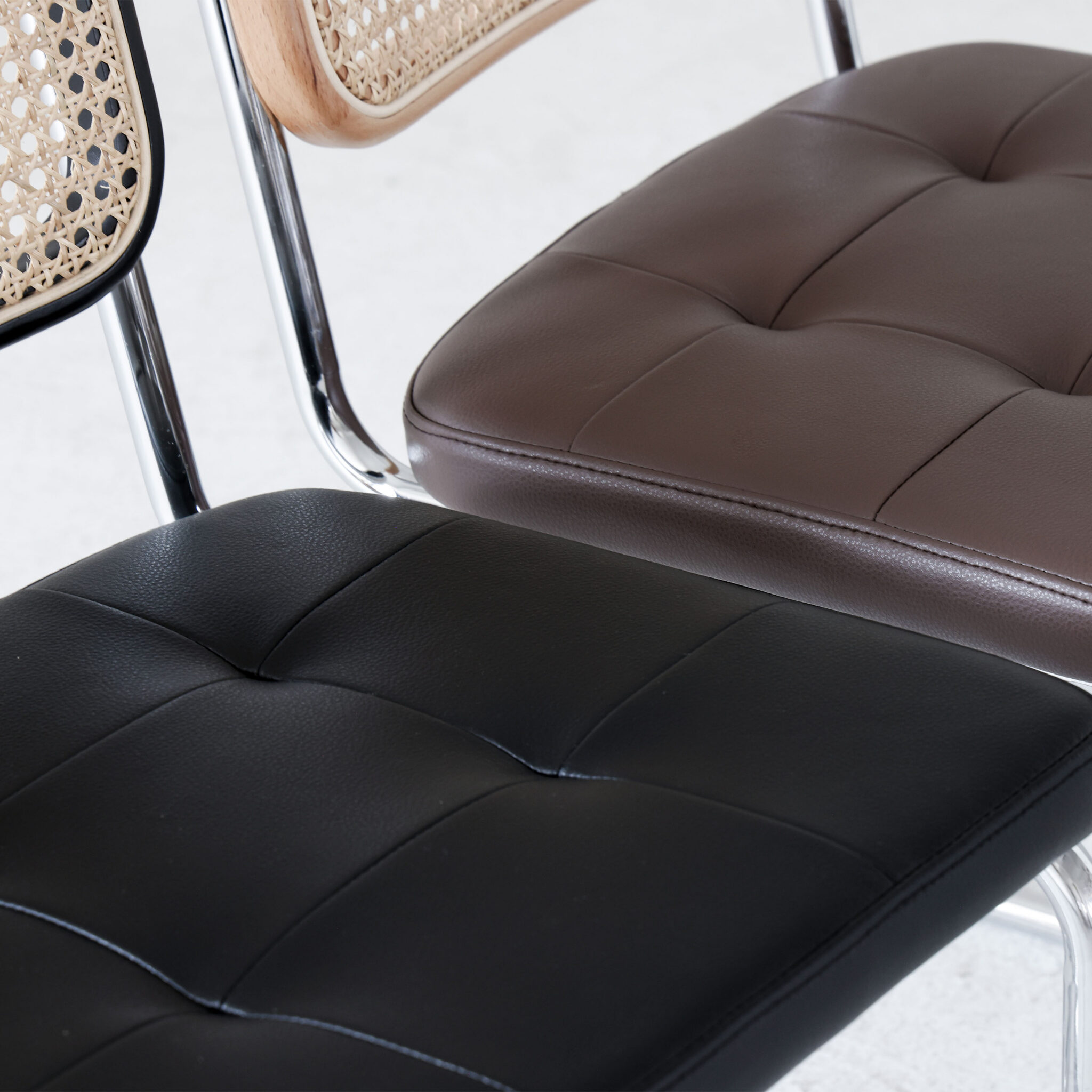 Close-up of three modern chairs with chrome legs; one has a woven cane backrest and brown cushion, the other two have tufted cushions in black and brown faux leather. All are placed on a light-coloured floor.